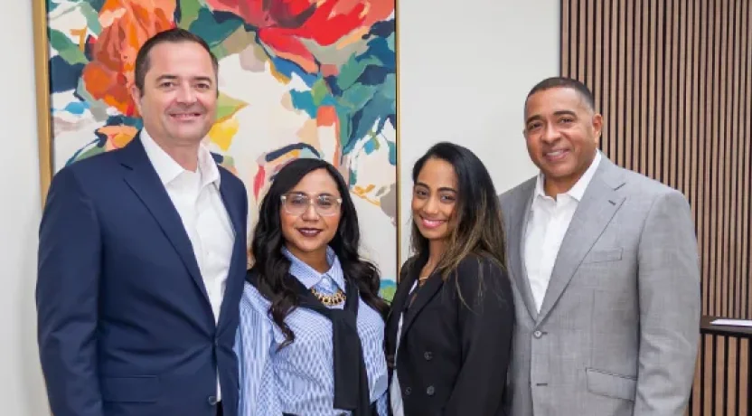 Four people in business attire posing in front of a colorful painting
