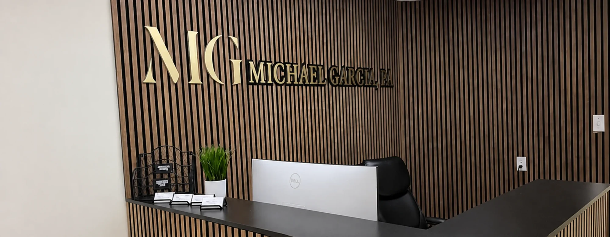 Reception desk of the Michael Garcia, P.A. office, the firm's gold MG logo on a wood-slat wall